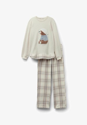 Maglietta da pigiama a maniche lunghe color crema con un orsacchiotto che indossa un maglione e un cappello blu, abbinata a pantaloni da pigiama a quadri beige e blu.