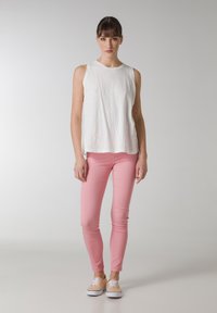 Vit ärmlös topp, mjukt material, rundad nederkant; rosa tajta byxor, stretchy tyg; bruna sneakers med vita sulor, snörningsdesign.