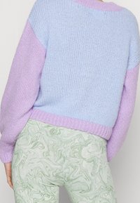 Sweter dzianinowy w jasnoniebieskie i lawendowe bloki, z prążkowanymi mankietami i dołem. W parze z zielonymi leggingsami marmurkowymi z falistym wzorem.
