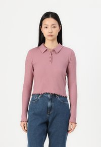 Rosa ribbestrikket langermet polo med kragehals, med knappelukking og slitt kant, sammen med høytlivede blåjeans.