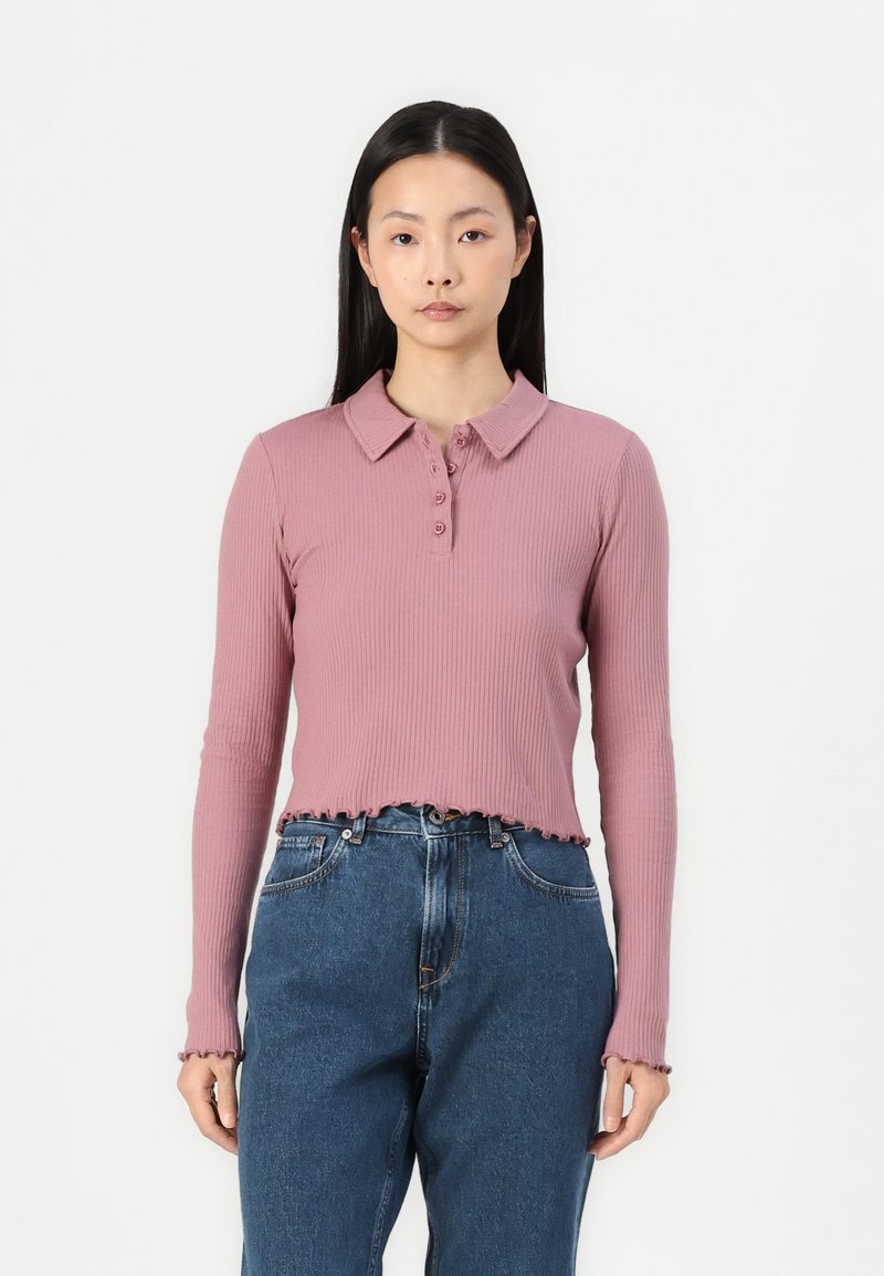 Rosa ribbestrikket langermet polo med kragehals, med knappelukking og slitt kant, sammen med høytlivede blåjeans.