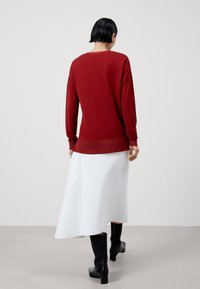 Rode gebreide trui met lange mouwen, gecombineerd met een witte midi-rok. Zwarte laarzen met hak maken de look compleet. Soepele texturen, comfortabele pasvorm.