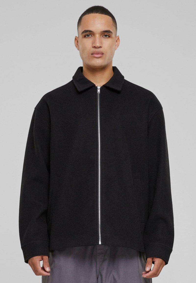 Black zip-up jacket with a collared neckline, relaxed fit, and side pockets, made from smooth fabric with a textured surface.