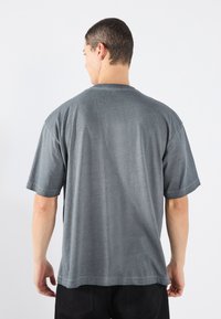 Graues kurzärmliges T-Shirt mit Rundhalsausschnitt, aus leichtem Stoff und mit glatter Textur. Es hat eine entspannte Passform und ein einfaches Design.