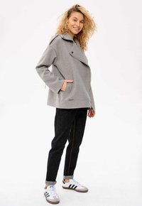 Szary płaszcz z wełny z szerokimi klapami, kieszeniami bocznymi i luźnym krojem, w zestawieniu z ciemnymi dżinsami i białymi sneakersami Adidas.