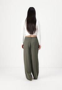 Pantalons ample en tissu vert olive avec une finition mate, comportant deux poches arrière et une taille ajustée.