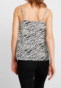 Camiseta sin mangas de estampado de cebra en blanco y negro con tirantes finos, diseño fluido y tela suave, con un dobladillo recto y textura ligera.