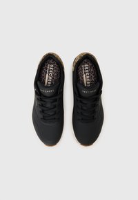 Black athletic shoes with a textured surface, lace-up design, and a leopard print insole. Rubber outsole for traction.