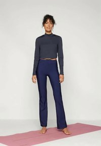 Mørkeblå yogabukser med utslåtte ben og høy midje, paret med en tettsittende mørkegrå langermet topp, brukt på en rosa matte.
