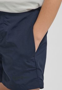 Jūras zili šorti ar gludu tekstūru, aprīkoti ar sānu kabatām un diskrētu Jack Wolfskin logo apakšējā kreisajā pusē.