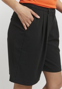 Schwarze, maßgeschneiderte Shorts mit Vordertaschen und lockerem Schnitt, gefertigt aus glattem Stoff mit einem sauberen, minimalistischen Design.