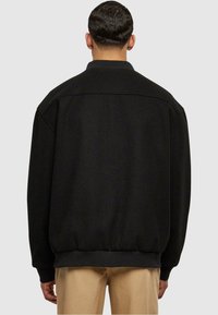 Chaqueta de forro polar negra de gran tamaño con cuello, puños acanalados y dobladillo. Textura suave con un diseño minimalista, vista desde la parte posterior.