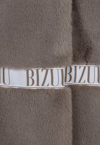Bruine nepbont stof met een zachte textuur, voorzien van een witte band met "BIZUU" gedrukt in lichtbruine letters over het midden.