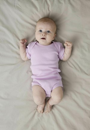 Šviesiai purpurinė ripsinė jumpsuit su trumpomis rankovėmis ir spaustukais apatėje, guli ant neutralaus atspalvio fono. Akys plačiai atmerktos.