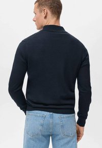 Dunkelblauer Pullover mit langen Ärmeln und Polo-Kragen, mit gerippten Bündchen und Saum. Getragen mit hellblauen Jeans aus Denim, die eine glatte Textur aufweisen.
