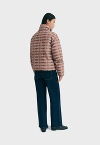 Padded jacket with a checker pattern in pink and green, featuring a high collar and a relaxed fit, paired with dark blue wide-leg jeans.