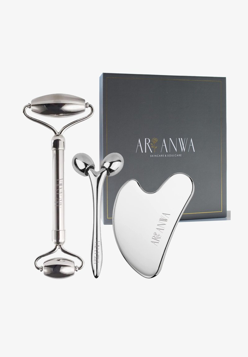 Trois outils de massage facial en argent avec la marque Aranwa exposés à côté d'une boîte gris foncé étiquetée "Aranwa Skincare & Soulcare."