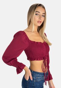 Haut court rouge à manches bouffantes, design smocké, encolure carrée et détail noué à la taille, assorti à un jean bleu.