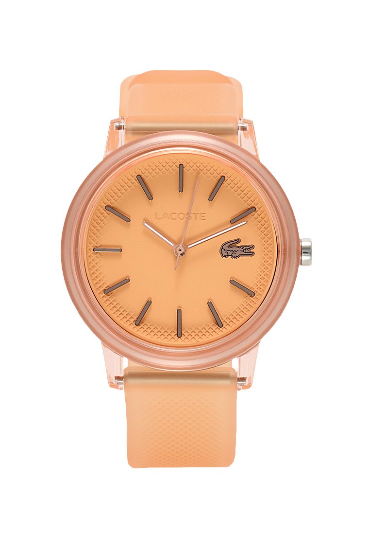 Reloj de plástico color melocotón con una esfera redonda texturizada, marcadores de horas minimalistas en negro y una correa de silicona a juego. Logo de Lacoste exhibido.