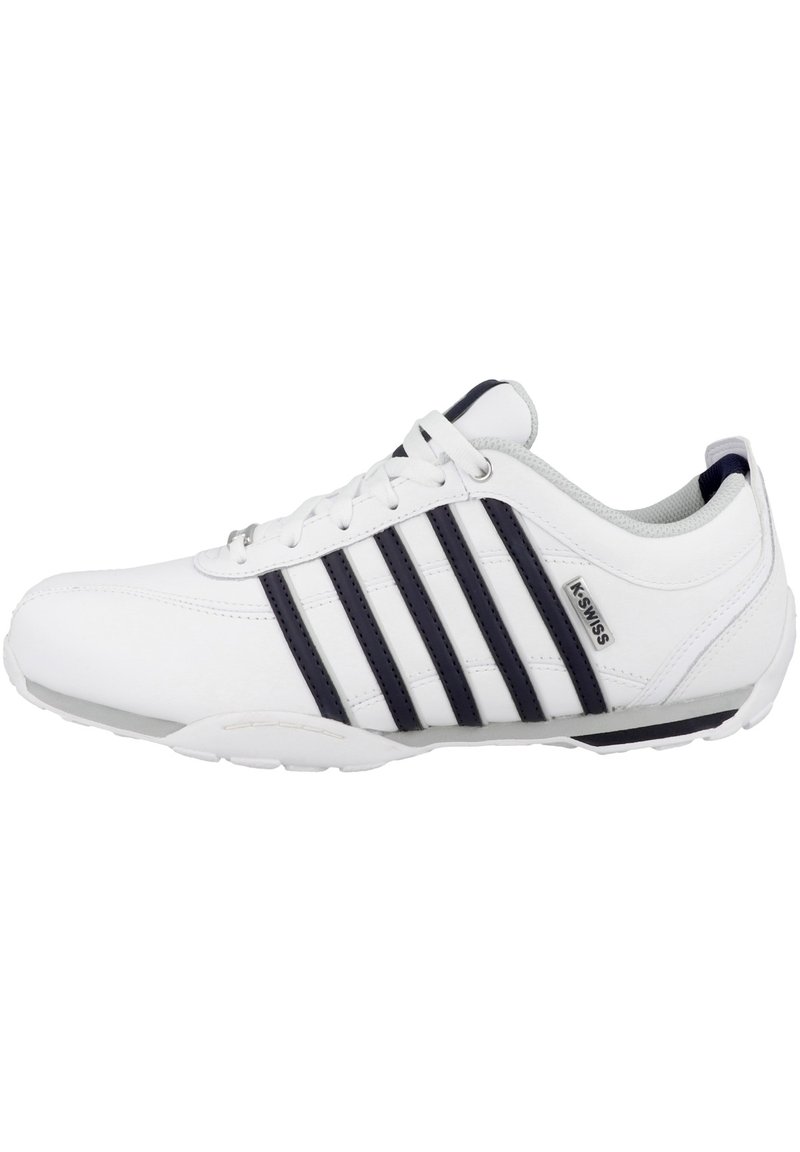Weiße Sportschuhe mit einem glatten Lederoberteil, das drei dunkelblaue Streifen aufweist, einem gepolsterten Kragen und einer flexiblen weißen Sohle.