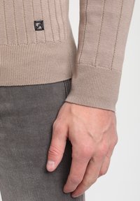 Beidzs ribu adīta džemperis ar teksturētu adījuma rakstu, kurā ietilpst audumam ieausts logotipa uzlīme. Fitēti piedurkņu gali un apakšdaļa ar kontrastējošu austa tekstūru.