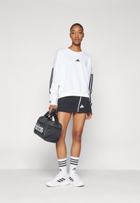 Hvitt genserskjorte med tre svarte striper på ermene, kombinert med et svart miniskjørt. Svart treningsbag, hvite sko og stripete sokker.