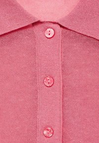 Gros plan d'un vêtement tricoté rose avec un col et trois boutons roses assortis sur le devant.