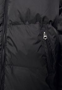 Svart puffjacka med en sidoficka med silverdragkedja, madrasserad textur och lättviktigt tyg med en subtil glans.