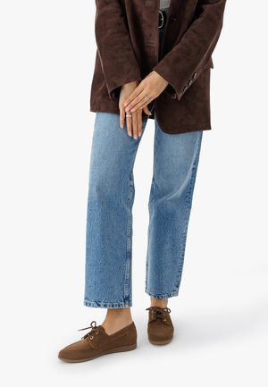 Blazer de ante marrón sobre una blusa gris claro, combinado con jeans de mezclilla azul de cintura alta y zapatos de cordones marrones.