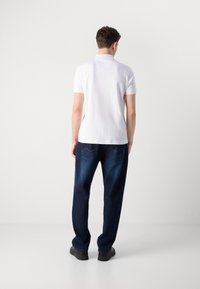 Hvit kortermet polo skjorte brukt med mørkeblå løse jeans i denim. Jeansene har et distinkt søm-mønster på baklommene.