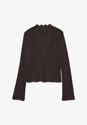 Smeđa skraćena majica izrađena od teksturiranog materijala. Ima duge rukave i izrez u obliku valovitog V-izreza. Dizajn ima slojeviti valoviti uzorak.