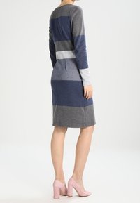 Långärmad stickad klänning med horisontella ränder i grått, marinblått och vitt. Figursydd design, knälång och en diskret söm bak.