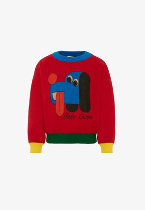 Maglione rosso lavorato a maglia con una grafica di un cane blu con la lingua di fuori. Accenti in blu, verde e giallo sul colletto e sui polsini.
