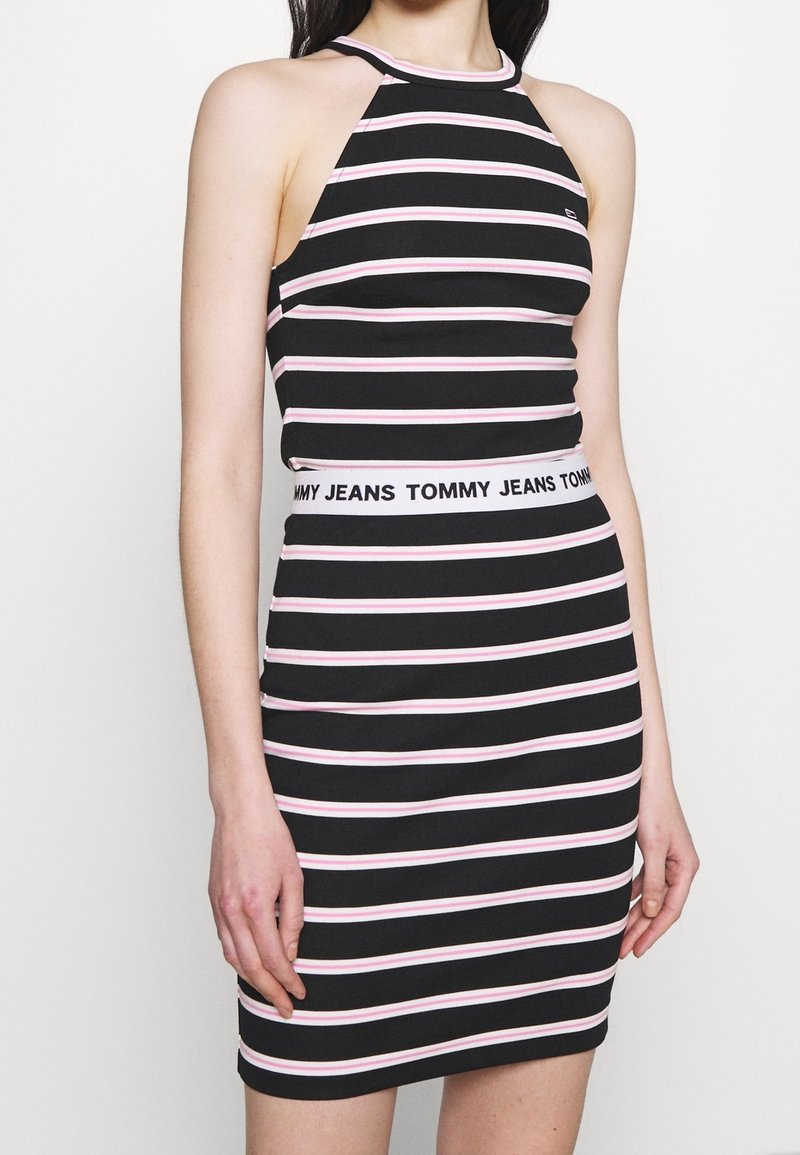 Czarna i różowa w paski bezrękawnikowa sukienka o wysokim dekolcie i dopasowanym kroju; posiada białą wstawkę z napisem "TOMMY JEANS" w talii.