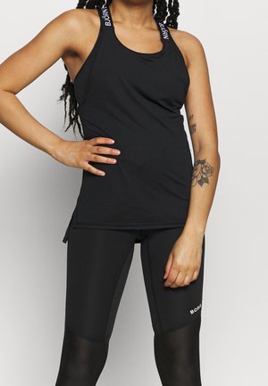 Musta urheilullinen tankkitoppi racerback-mallilla ja brändätyillä olkaimilla, yhdistettynä mustiin, istuviin shortseihin, joissa on verkkoyksityiskohtia ja logot.