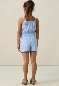 Rompers rayé bleu avec fines bretelles et taille élastique. Comprend un short et une coupe décontractée. Les chaussures sont des sandales brunes avec des boucles.