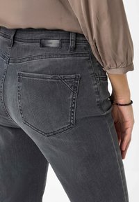Grijze denim spijkerbroek met een middelhoge taille, uitgerust met een achterste linkse zak en subtiele stikseldetails. Het materiaal lijkt zacht met een lichte stretch.
