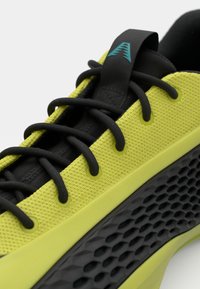 Scarpa da ginnastica verde lime con una parte superiore testurizzata, lacci neri e una distintiva suola in gomma nera con un motivo a nido d'ape.