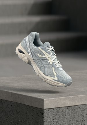 Chaussure de sport gris clair avec tige en mesh, col rembourré et accents crème contrastants ; dispose d'un design de semelle unique et de surfaces texturées.