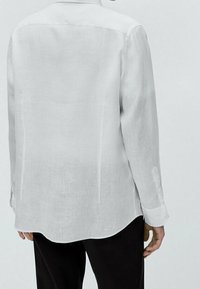 Witte linnen blouse met lange mouwen, een klassieke kraag en een afgeronde zoom; de stof lijkt lichtgewicht en iets doorschijnend.