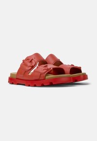 Red rubber sandals featuring dual adjustable straps, a cushioned footbed, and a thick, textured sole with a rugged tread design.