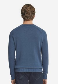 Blå stickad tröja med rund halsringning och ribbad nederkant. Har långa ärmar och en jämn textur, visas bakifrån.