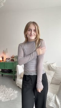 Szürke, hosszú ujjú felső magas gallérral, amely áttetsző anyagból készült, kis fehér pöttyökkel díszítve. Fekete nadrág van rajta.