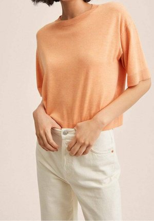 Suéter corto de manga corta en una mezcla de algodón de color naranja claro, combinado con jeans de tiro alto en color crema que cuentan con cierre de botón y bolsillos.