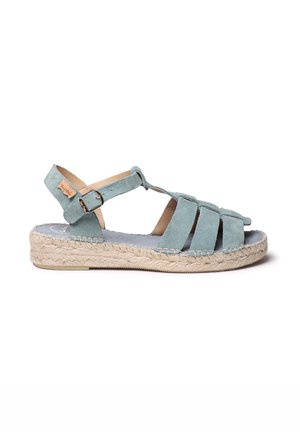 Gai zila zamšas sandāle ar sakrustotām siksnām, espadrille zoli un potītes siksnu ar sprādzi. Strukturēts jūtu detaļas elements zoles apakšā.