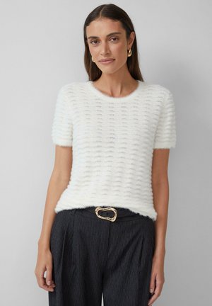 White, textured short-sleeve sweater with a wavy pattern; paired with dark striped pants and a gold belt buckle accent.