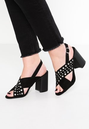 Sorte ruskind hæle sandals med en stropdesign, dekoreret med sølvnitter, åben tå og blokhæl. Accentueret med justerbare ankelremme.