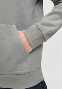 Sudadera gris claro con un bolsillo tipo canguro, puños y bajo acanalados. Textura suave y grosor medio, adecuada para uso casual.