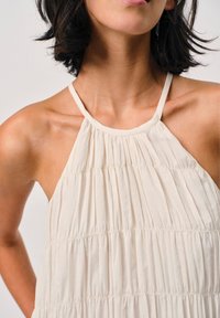 Elfenbeinfarbenes Halsband-Top aus strukturiertem, gerafftem Stoff. Es hat dünne Träger und eine lockere Passform, die ein leichtes, fließendes Design betont.