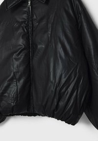 Giacca bomber in ecopelle nera con una finitura lucida, dotata di chiusura con zip e orlo elasticizzato. Maniche ampie e design con colletto classico.
